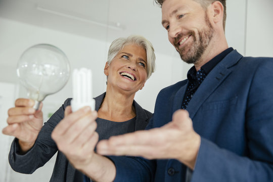 Businesswoman and businessman comparing regular and energy-saving lightbulb