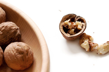 Single cracked open half walnut and several full walnuts on plate, white isolated background