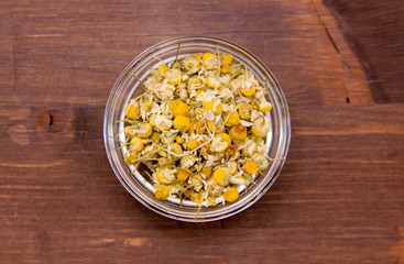 Chamomile flower on bowl on wooden table seen from above