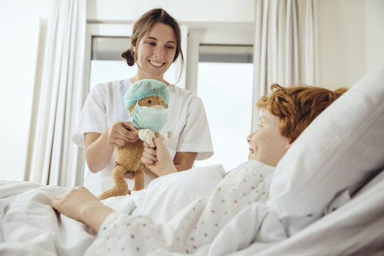 Boy in hospital bed receiving toy from nurse