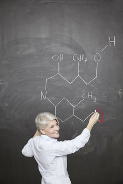 Female teacher drawing chemical formula on blackboard