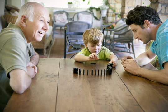 Little boy playing with his father and grandfather domino