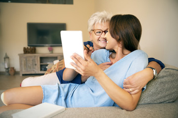 Happy senior woman and adult daughter on couch with digital tablet