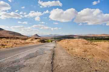 Broken asphalt road in the dry grass valley under white clouds and mountain range