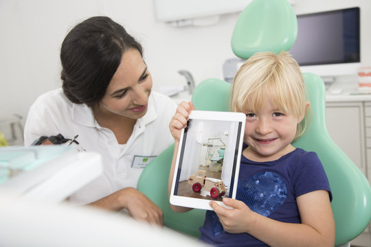 Dentist and smiling girl showing digital tablet in dentist's chair