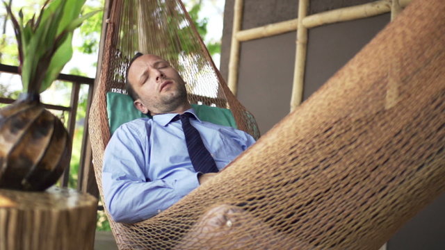 Young businessman sleeping on hammock on terrace
