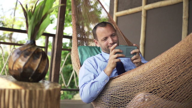 Happy businessman playing game on smartphone on hammock, super slow motion 240fps
