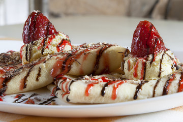 Two folded crepes with sweet filling served on a white plate with parfait cream, strawberries, hazelnuts and chocolate. 