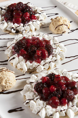 Portion of crepes stuffed with hazelnut cream and mixed fruit, cherry, sour cherry, currant, strawberry, blackberry and decorated with whipped cream, served on a white plate.