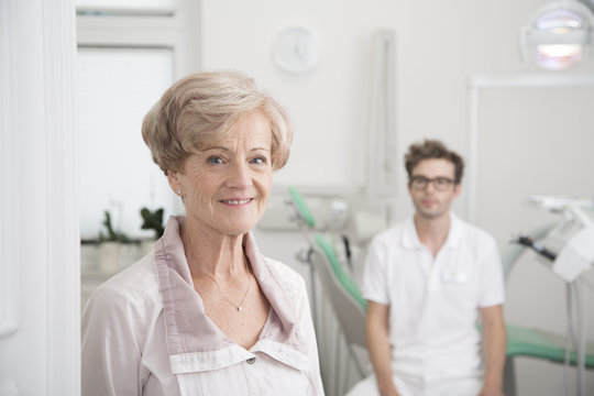 Portrait of smiling senior woman in surgery with dentist in background