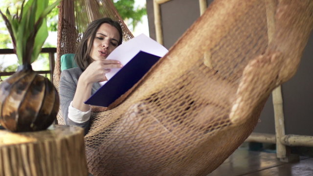 Young businesswoman reading documents lying on hammock on terrace
