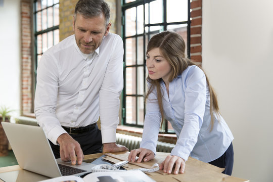 Mature man and young woman working together at tailoring shop