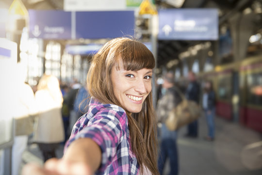 Germany, berlin, portrait of smiling young woman holding hands at platform
