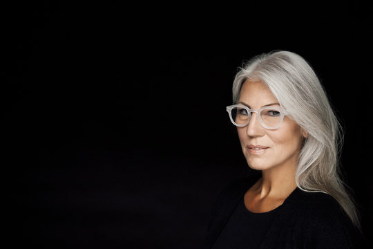 Portrait of mature woman with grey hair wearing glasses in front of black background