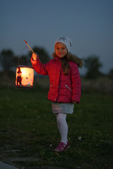 Portrait of smiling little girl with lighted paper lantern on St. Martin's Day at twilight