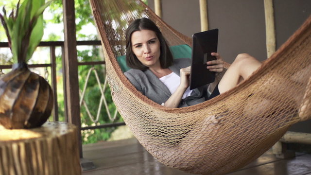 Friendly businesswoman with tablet talking good news on hammock
