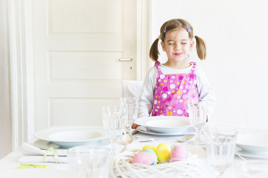 Portrait of smiling little with closed eyes girl standing behind laid table