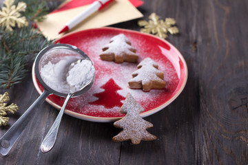 Homemade Christmas cookies in the shape of a Christmas tree, sprinkled with powdered sugar on a dark wooden table with festive decorations, selective focus 