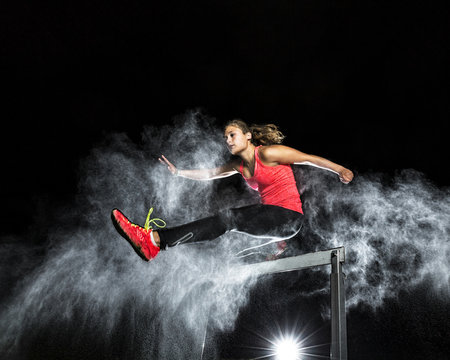 Young woman jumping over hurdle in between cloud of flour