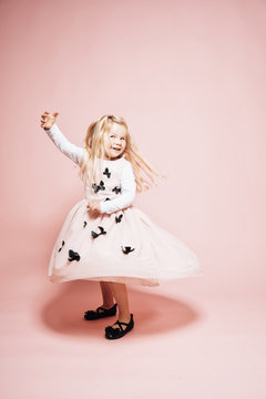 Smiling blond little girl dancing in front of pink background