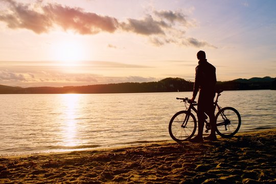 Young man cyclist silhouette on blue sky and sunset above the beach. Biker atthe end of season at lake.
