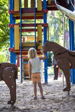 Little girl standing on playground stroking wood horse