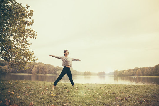 Woman doing a moon salutation yoga pose in autumn park