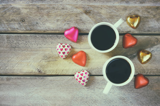 top view image of colorful heart shape chocolates, fabric heart and couple mugs of coffee on wooden table. valentine's day celebration concept
