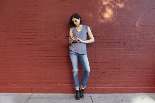 Portrait of woman with digital tablet leaning against red brick wall