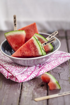 Bowl of melon popsicles and a bitten one on wood
