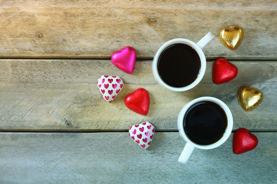 top view image of colorful heart shape chocolates and couple mugs of coffee on wooden table. valentine's day celebration concept. retro filtered image
