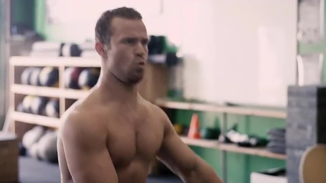 A fit young man doing squats with a kettle bell in a small gym