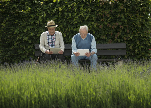 Two old men using tablet computers in the park