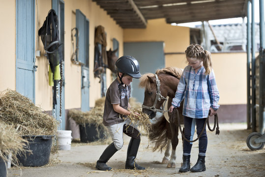 Germany, NRW, Korchenbroich, Boy and Girl at riding stable with mini Shetland pony