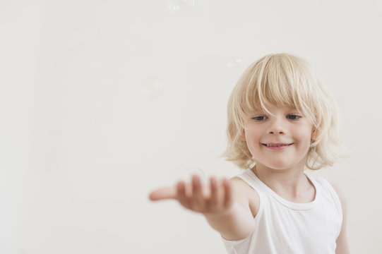 Portrait of smiling little boy with outstretched arm watching a soap bubble