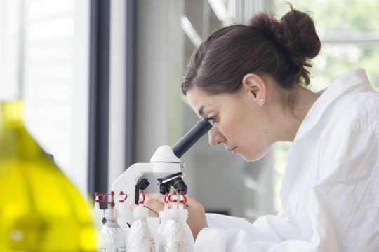 Portrait of young female chemist looking through microscope