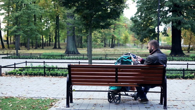 Man with stroller watching movie on tablet computer sitting in the park
