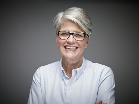 Portrait of laughing mature woman with grey hair in front of grey background