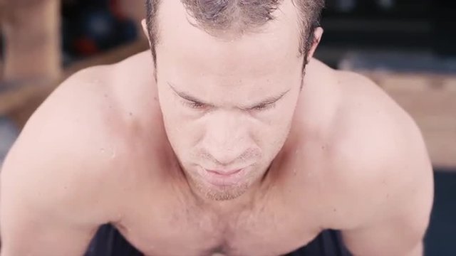 A fit young man with water dripping off of him after a workout looks up at the camera