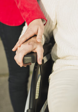 Young woman's hand on hand of senior woman sitting in wheelchair