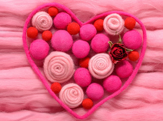The contour of the heart as a valentines. Filled with beads and a stylized roses made of wool in different shades of pink. Background made of wool for felting