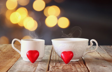 image of two red heart shape chocolates and couple cups of coffee on wooden table in front of bokeh abstract background. valentine's day celebration concept
