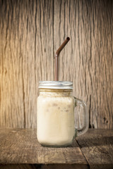 Iced coffee with milk in vintage jar on wood background