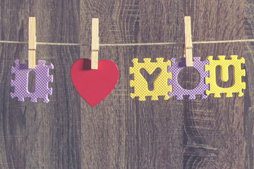 Love concept. Red heart and letters (forming I Love You message) hanging on a clothesline against a wooden background