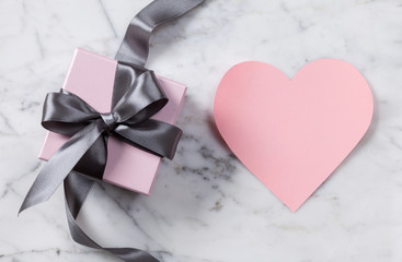 Pink heart and gift box with a gray silk ribbon and bow on a marble background