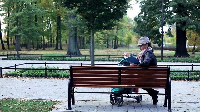 Woman with stroller reading book in the park
