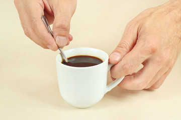 Hands mixing with a spoon of hot coffee in the cup
