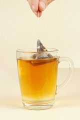 Hand brews pyramid tea bag in a glass of hot water