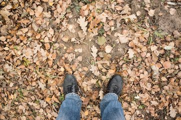 Male feet in blue jeans and black shoes on dirty ground