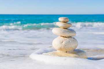 Fototapeta na wymiar Stones pyramid on sand symbolizing zen, harmony, balance. Ocean